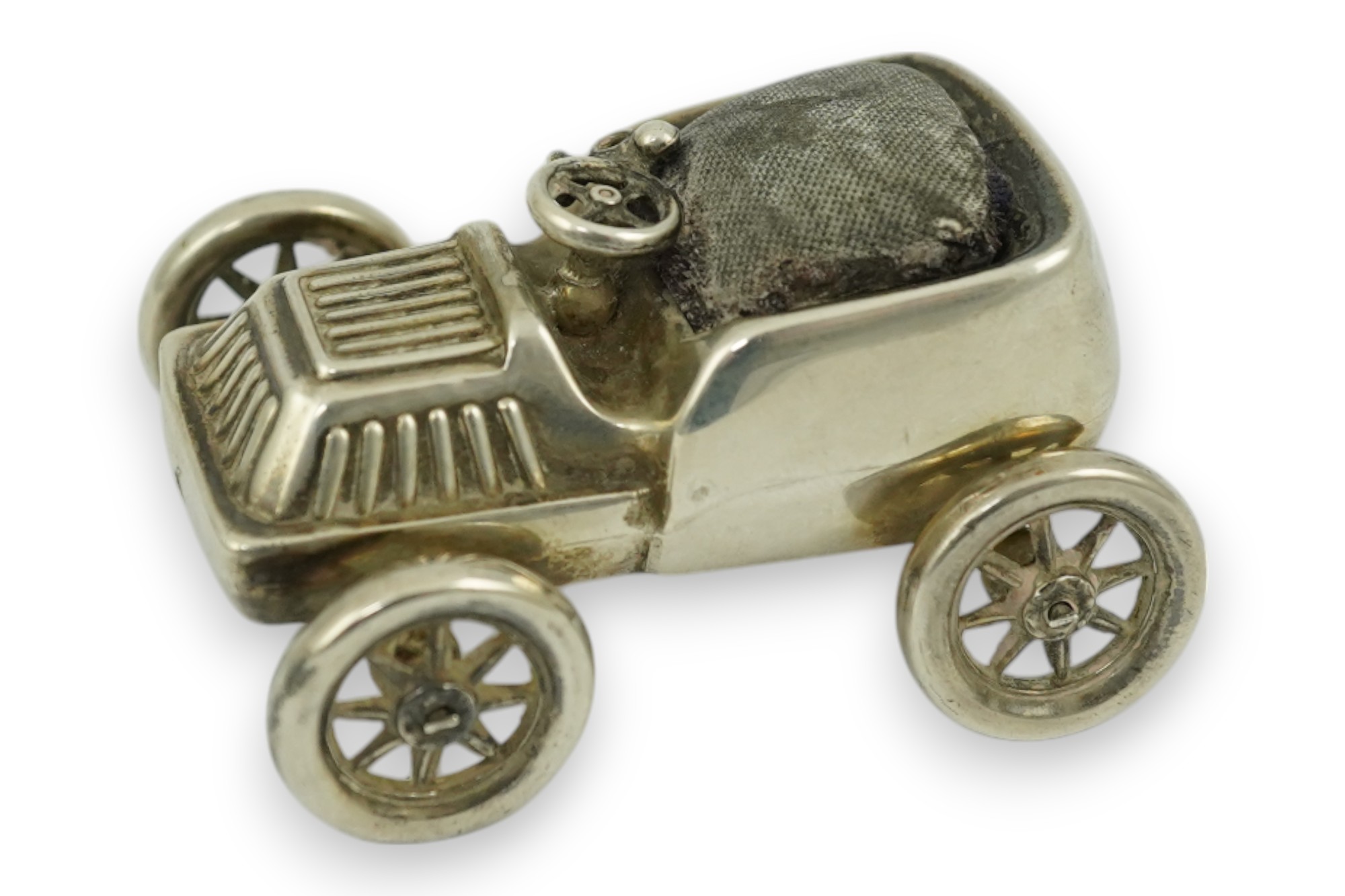 An Edwardian novelty silver mounted pin cushion modelled as a vintage car, makers mark rubbed, Birmingham, 1906, 57mm. Condition - poor to fair